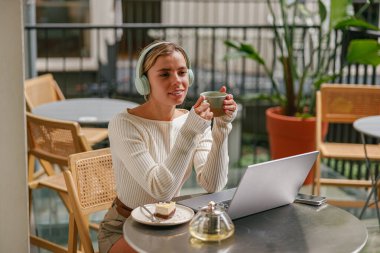 Canlı ve canlı bir kafe ortamında şık bir kadın laptopuna odaklanırken kahvesini yudumlamaktan hoşlanır.
