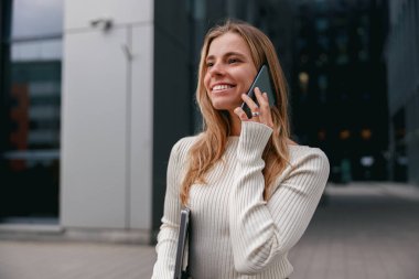 Şık ve şık bir şehir ortamında telefon görüşmesi yapan genç bir kadın mutlu bir şekilde gülümsüyor.