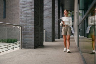 Gündelik giyinmiş genç bir kadın, hareketli modern kentsel alanlarda rahatça dolaşır.