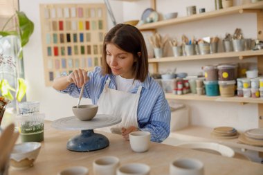 Yetenekli bir sanatçı, yaratıcı aletler ve malzemelerle dolu parlak bir çalışma alanında çömleği ustalıkla şekillendirir.