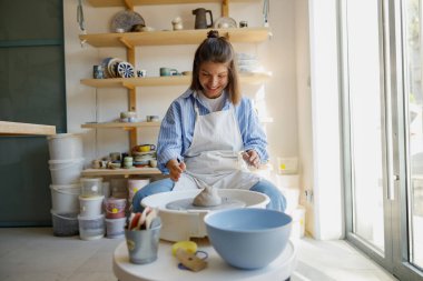 Bir kadın, parlak ve ilham verici bir stüdyoda çömlek çarkında güzel bir kil parçasını neşeyle şekillendiriyor.