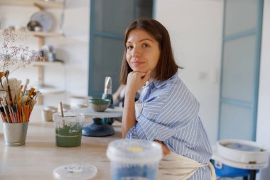 Kendini işine adamış bir sanatçı, iyi ışıklandırılmış ve canlı bir stüdyo alanı içinde özenle çömlek yaratma sanatıyla ilgilenir.