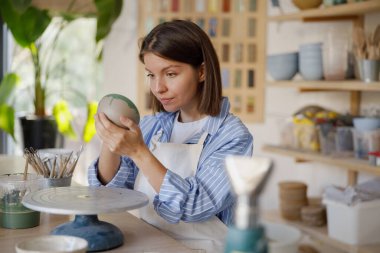 Kendini işine adamış bir kadın, zengin kil ve malzemelerle dolu ilham verici bir stüdyoda güzel çömlekler yapıyor.