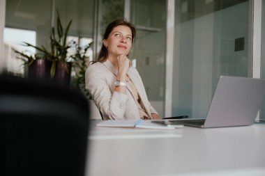 Bir iş kadını, bir sonraki adımlarını ve seçimlerini düşünceli bir şekilde modern bir ofiste değerlendirip seçeneklerini değerlendiriyor.