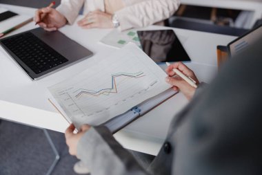 Finansal analizleri ve tartışmaları çizelgeler ve dizüstü bilgisayarlar üzerinden gösteren ortak bir iş sahnesi.