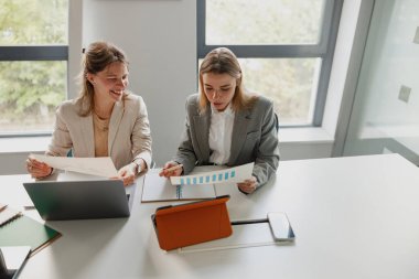 Parlak bir ofiste, iki kadın analiz için grafikler ve cihazlar kullanarak etkili iş stratejilerini tartışıyor