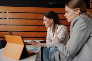 İki kadın, modern bir çalışma alanında etkili bir tablet kullanarak iletişim ve fikirlerini destekliyor.