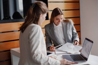 İki iş kadını, şık bir ofis ortamında önemli belgeleri incelerken bir projeyi tartışıyor.