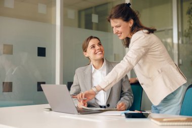 İki yetenekli profesyonel kadın, bir dizüstü bilgisayar üzerinde çalışırken modern ofis ortamında etkin bir şekilde işbirliği yapıyorlar.