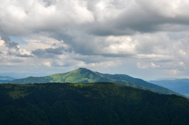 Beautiful summer landscape with forested hills, mount Strymba in the distance, and sky with low clouds. Carpathian mountains, Ukraine