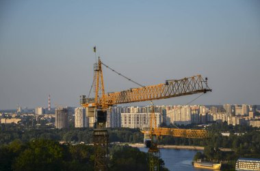 Two high construction cranes with Dnipro river and left bank city districts on the background. Urban skyline of Kyiv, Ukraine 
