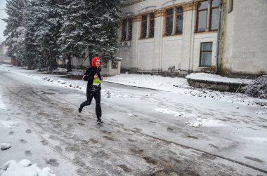 KYIV, UKRAINE - NOVEMBER 27, 2022: View of young man running in winter time and snow in running competition. Male athlete in running outfit sprinting frosty weather.