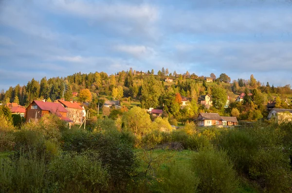 Picturesque sunny autumn scenery of rolling countryside with rural houses of a small village on green and yellow hills. Slavske, Carpathian Mountains, Ukraine
