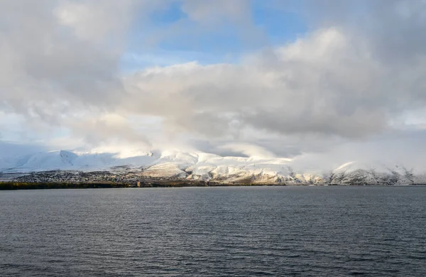 Dark water surface of Sevan Lake and mountain chain covered by snow and clouds over the lake. Armenia