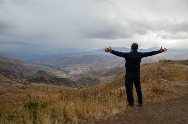 Seyyah adamın arka plandaki dağlara doğru ellerini kaldırması ve manzaranın keyfini çıkarması. 