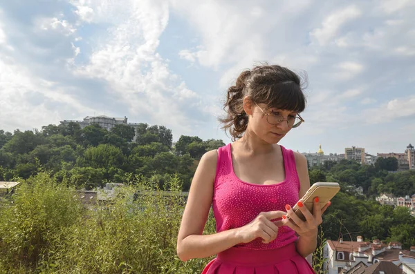 Молодая Брюнетка Очках Розовом Платье Читает Смотрит Свой Мобильный Телефон — стоковое фото