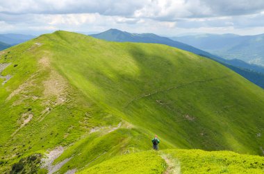 Sırt çantalı bir adam güzel yeşil dağ sırtı arka planında yolda yürüyor.