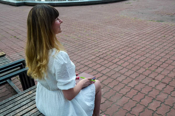公園のノートに座っている若い女性の後部ビューと彼女の手にペン 少女は仕事や勉強をする — ストック写真