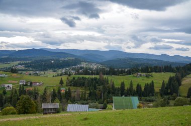 Yükseklikten manzara çok güzel. Bulutlu gökyüzünün altındaki orman ve dağlarda tipik bir Karpat köyü. Karpatlar, Ukrayna