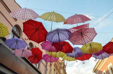 Gökyüzüne karşı caddenin üzerinde parlak ve renkli asılı şemsiyeler. çok renkli sokak dekorasyonu