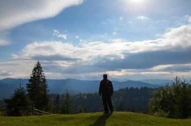 Sırt çantalı bir yürüyüşçü tepeden aşağıdaki vadiye ve çok uzaktaki dağlara hayranlıkla bakıyor. Seyahat ve aktif yaşam tarzı
