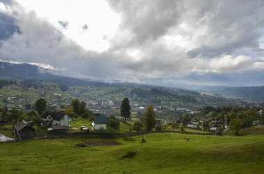 Dağlar ve Vorokhta köyü arasında uzanan görkemli, fırtınalı bulutlu gökyüzü altında geniş bir vadi manzarası. Karpatlar, Ukrayna