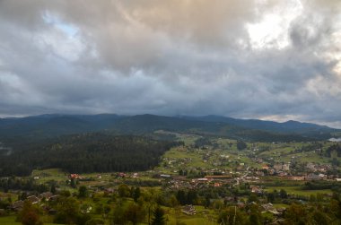 Vorokhta dağ köyünün panoramik manzarası. Yeşil tarlaları, ağaçları, evleri ve arka planda dağları olan kırsal alan. Karpat Dağları, Ukrayna.