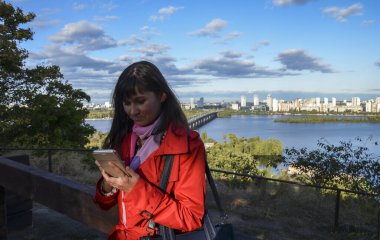 Şehir arka planında akıllı telefonu olan kırmızı ceketli esmer kız. Halk yaşam tarzı konsepti