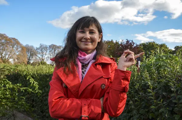 Kırmızı ceketli, gülümseyen ve elinde anahtarlarıyla gülümseyen esmer kadın. Araba ya da ev kirası