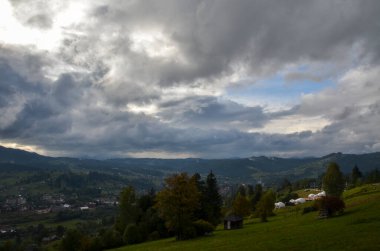 Glamping kubbesi, bulutlu gökyüzüne karşı dağlarla çevrili bir vadideki köyün manzaralı bir yamaçta çadır kurar. Karpatlar, Ukrayna