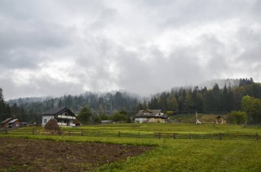Sonbahar sisiyle kaplanmış ormanlı dağ sırtlarının yanındaki kır evleri. Karpat Dağları, Ukrayna