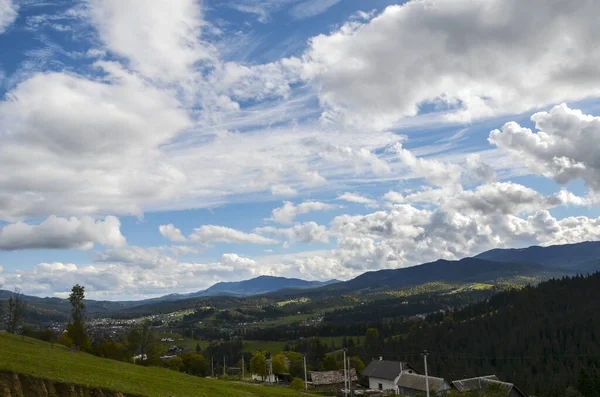 stock image Summer landscape with cozy village houses in the valley, trees on the hillsides and clouds on the blue sky above the distant ridge. Carpathian Mountains, Ukraine