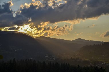 Uzak dağların tepelerinde gün batımı ışınları vadideki Karpat köyünün güzel manzarasını aydınlatıyor.