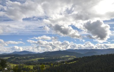 Tepelerde küçük evleri olan Karpat köyünün manzaralı manzarası. Arka planda yeşil ladin ormanları ve dağları vardı.