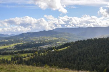Tepelerde küçük evleri olan Karpat köyünün manzaralı manzarası. Arka planda yeşil ladin ormanları ve dağları vardı.