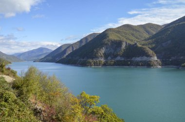 Güneşli bir günde yoğun yeşil dağlarla çevrili Zhinvali rezervuarının turkuaz su yüzeyi. Gürcistan 'ın resimli manzaraları