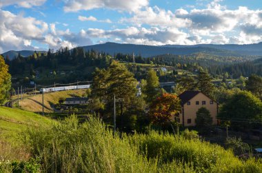 Vorokhta köyünün pitoresk manzarası boyunca esen tren, güneş ışınları altında bol yeşillikler arasında dağılmış çeşitli küçük evlerden oluşuyor. Karpat Dağları, Ukrayna
