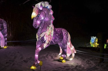 Gece manzarasını aydınlatan sihirli at şeklindeki ışık figürlerinin görüntüsü karlar üzerinde parıldayan ışığın etkisini yaratıyor. tema parkları, festival veya dekoratif ışıklandırma