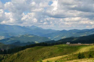 Tüylü bulutlarla dolu bir gökyüzünün altında küçük ahşap çobanların evinin olduğu yemyeşil dağların manzarası. Karpat Dağları, Ukrayna
