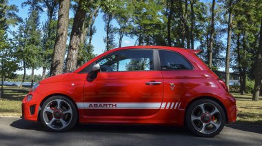 Canlı kırmızı Abarth 595 (Fiat 500) bir araba açık hava park, parlak tasarım ve spor estetik sergilenen yeşil ağaçlar ve açık gökyüzü karşı
