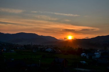Güneş, yuvarlanan tepelerin ardında batar, gün batımı gökyüzü, dağların arasına kurulmuş huzurlu bir köyün üzerinde ılık turuncu ve sarı tonlarla boyanır. Karpatlar, Ukrayna