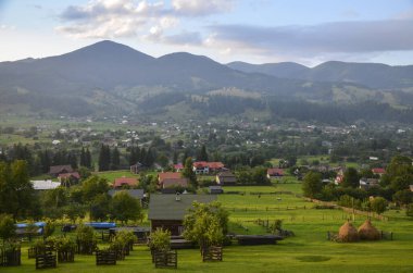 Kırsal alan dağınık evler, yemyeşil ağaçlar ve arka planda ormanlarla kaplı görkemli dağlarla süslenir. Verkhovyna, Karpatlar, Ukrayna