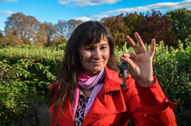 Kırmızı ceketli ve pembe eşarplı bir kadın yemyeşil arka planda anahtarı tutuyor. Fırsat kavramı ya da gayrimenkul, ev sahipliği gibi önemli bir şeyin kilidini açmak.