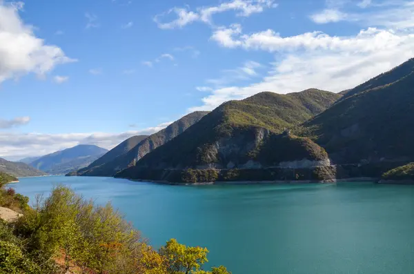 Stock image Turquoise water surface reflects the blue sky of Zhinvali Reservoir nestled amidst lush green hills or mountains. Travel to Georgia