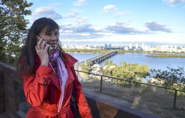 Güzel esmer kadın akıllı telefondan konuşuyor ve başka tarafa bakıyor. Kırmızı ceketli neşeli kız şehir planında cep telefonu kullanıyor..