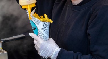 Eldiven takan pazarcı bir külah kızarmış patatesin üzerine sos dağıtıyor. Sokak yemekleri, fast food servisi ya da aşçılık etkinlikleri