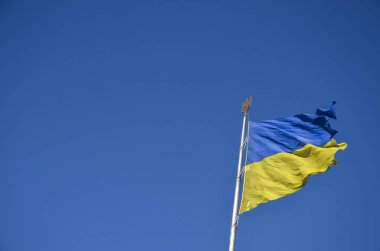 Mavi ve sarı bantlı Ukrayna çift renkli bayrağı, açık mavi gökyüzüne karşı üzerinde mızrak olan beyaz bir direğin üzerinde yükseliyor.