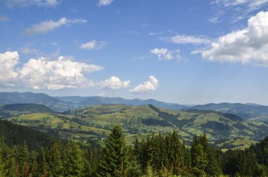 Summer landscape with village houses are scattered at the mountain hills are lush with greenery and trees under a clear blue sky with scattered clouds. Carpathian Mountains, Ukraine