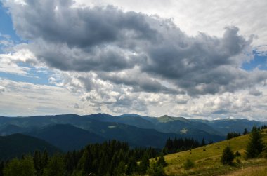 Önde yeşil ağaçlar ve arka planda çok katmanlı dağ sırtları olan sık ormanlarla kaplı yuvarlanan tepeler yer almaktadır. Ukrayna Karpatlarının dağlık bir bölgesinin nefes kesici manzarası