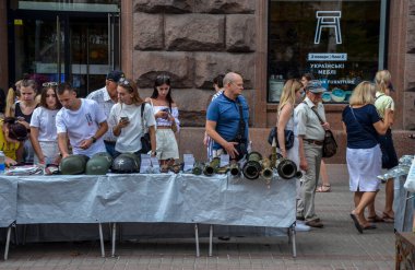 İnsanlar ele geçirilen miğferleri, el bombası fırlatıcılarını ve Rus işgalci güçlerinden alınan çeşitli askeri teçhizatı gözlemliyor.